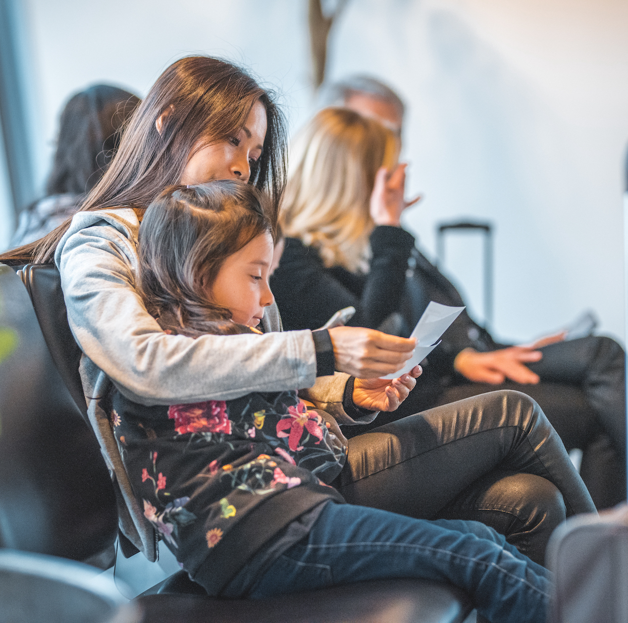 Mother and daughter reading airplane tickets while sitting on seats. Family is waiting at airport departure area. They are going on vacation.