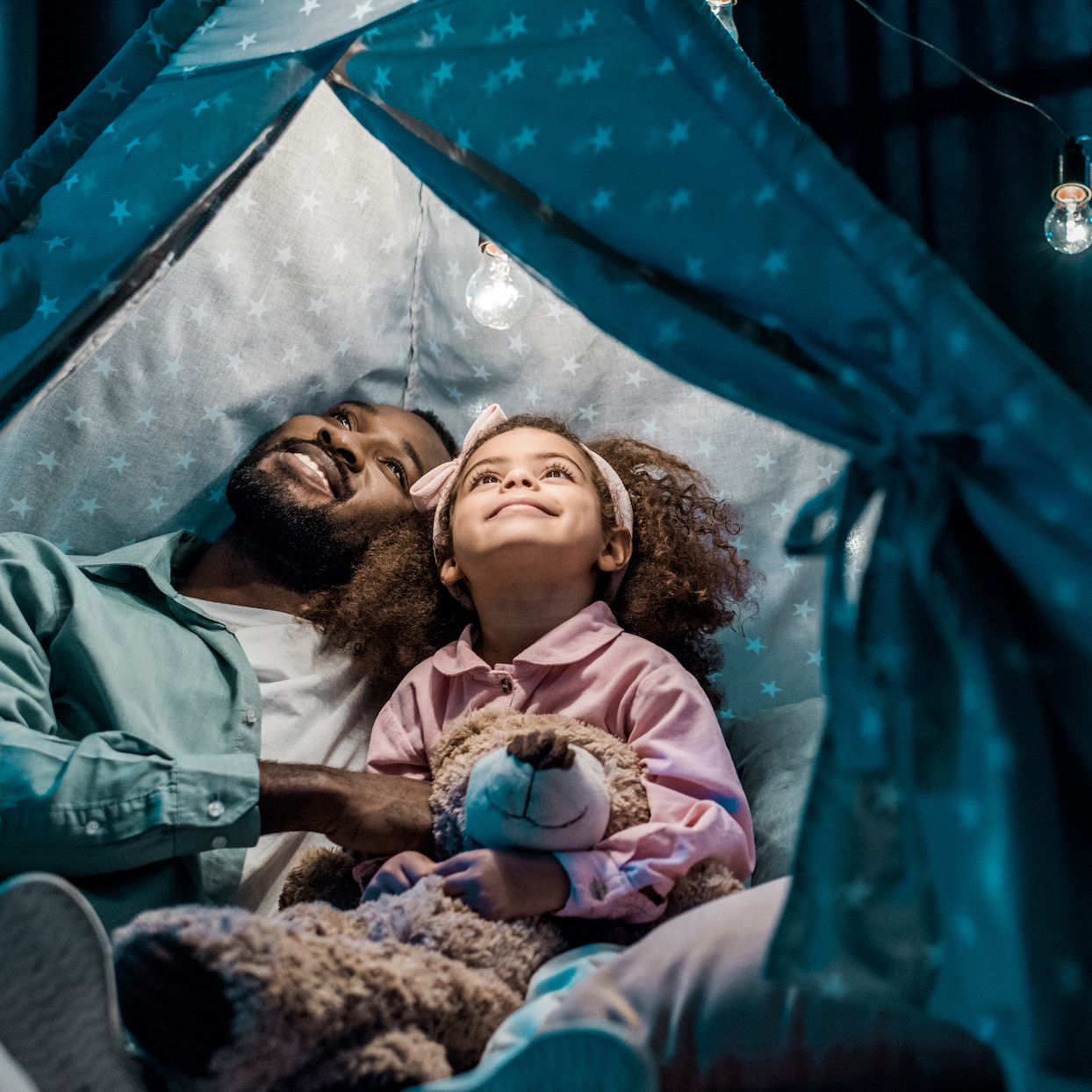 african american father looking up with daughter in wigwam in living room