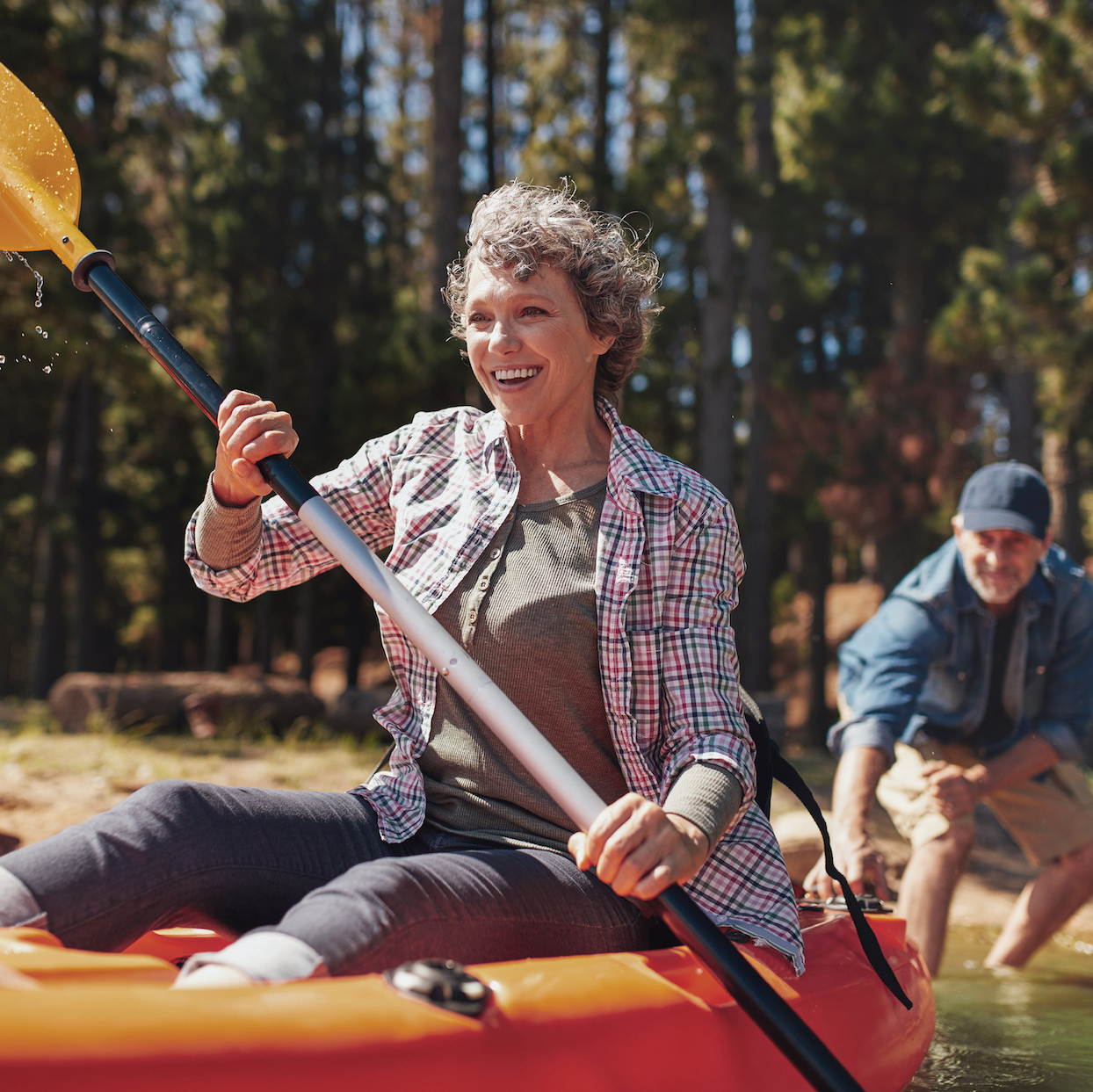 Portrait of happy senior paddling kayak in the lake with man supporting from behind. Mature couple enjoying a day at the lake.