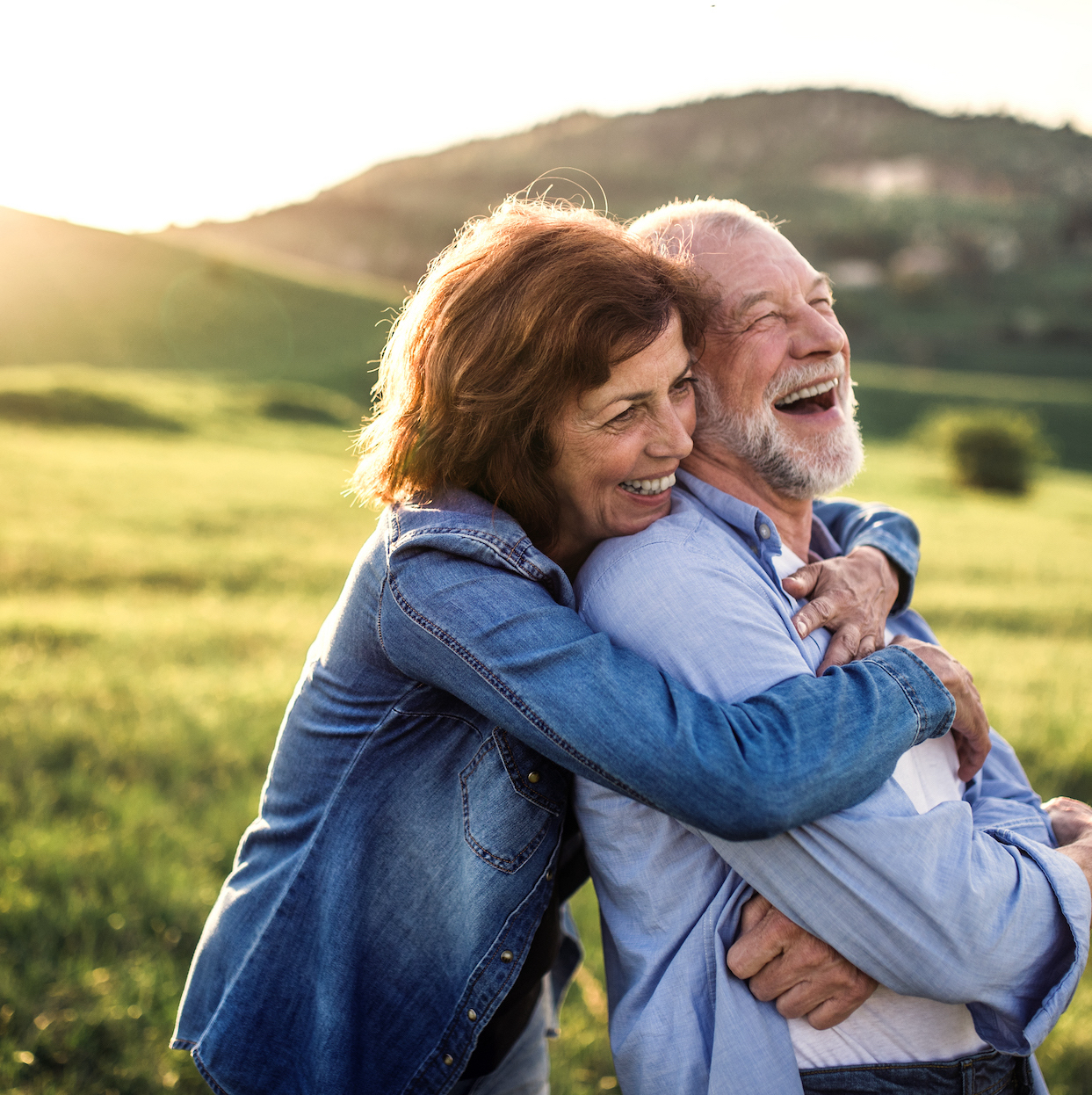 Happy senior couple outside in spring nature, hugging at sunset. Side view.