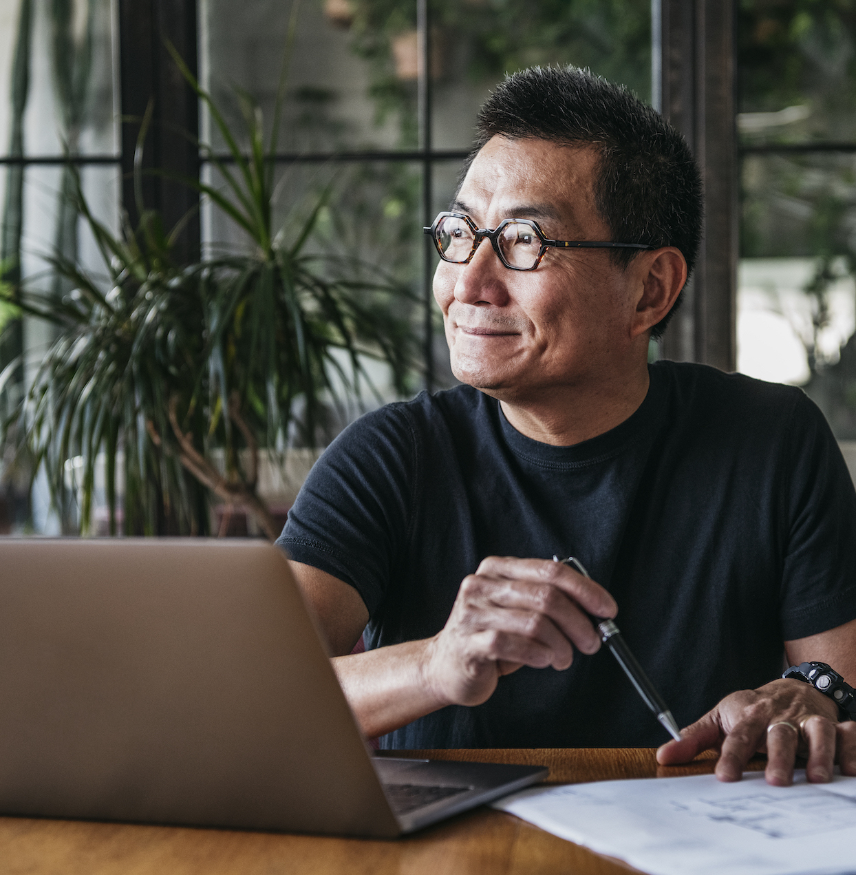 Cheerful man in his 50s sitting at table and looking away, doing paperwork, contemplation, ideas